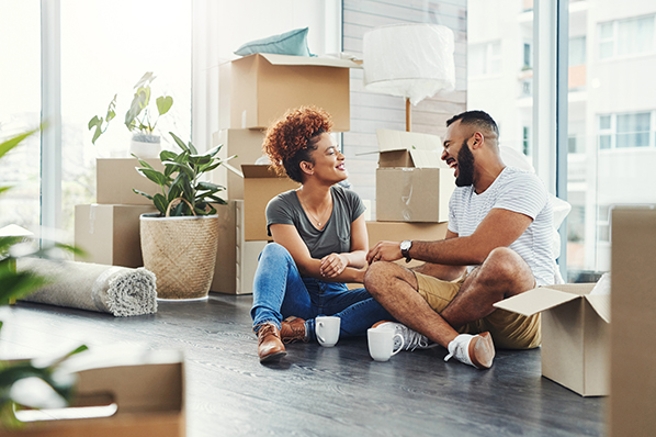 A couple sitting on the living room floor around carboard boxes