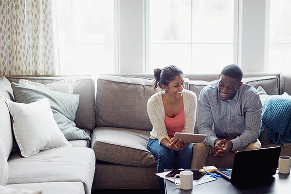 A couple sitting on a couch reviewing information on a notepad