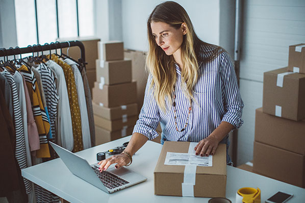 A woman browsing a laptop while packaging a box