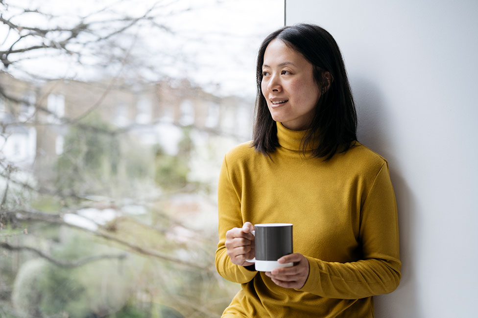 Woman holding a coffee while looking out a window