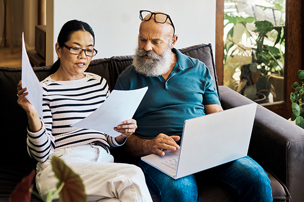 middle-aged couple looking at paper documents and their laptop