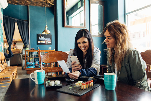 two women at a coffee shop looking at a smartphone screen