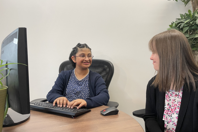 A woman and a girl sitting at a computer desk