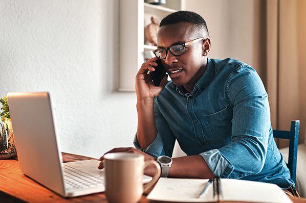 A man speaking a mobile phone while browsing a laptop